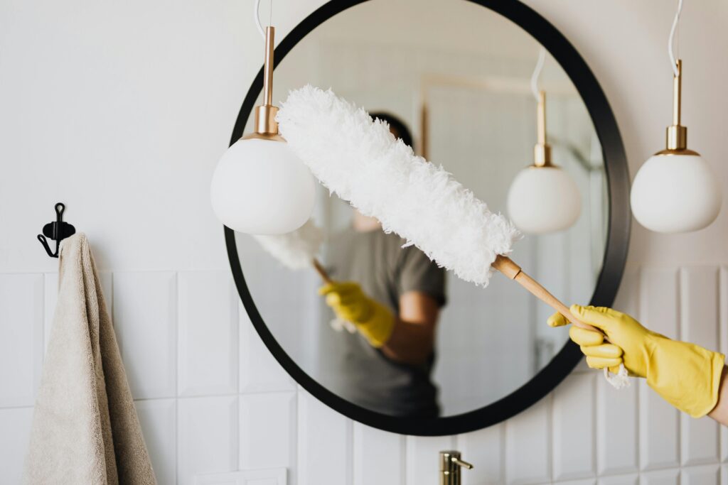 pexels-photo-4239031-4239031 A person cleaning an elegant bathroom mirror with a fluffy duster and yellow gloves.
